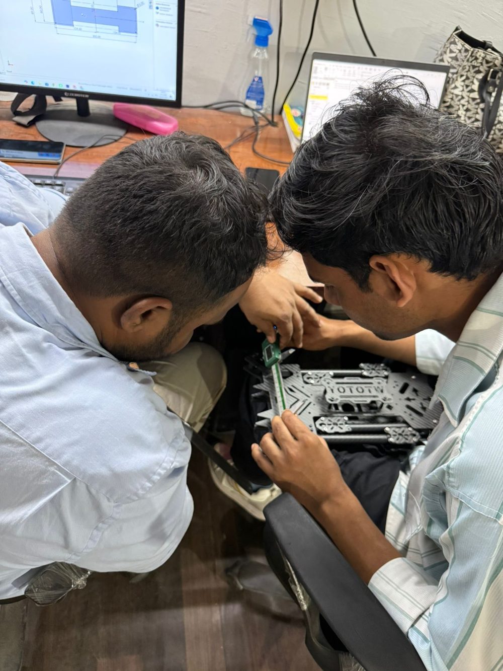 Two Aetherium Labs engineers measuring a carbon-fibre UAV frame with digital callipers